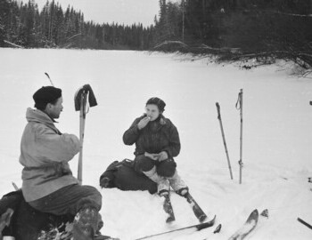Jan 28 - Halt on Lozva. Zolotaryov and Kolmogorova. A quilted jacket is attached to Zolotaryov's backpack. Visible are spare skis tied with ropes.